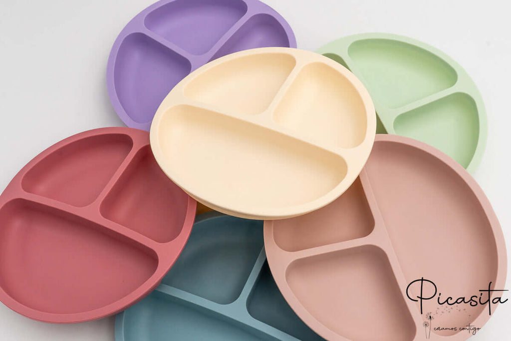 Conjunto de platos de silicona con compartimentos en colores lila, crema, verde, rojo, azul y rosa.
