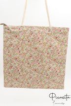 Bolsa de tela tipo tote bag con estampado de flores rosas y asas de cuerda blanca.