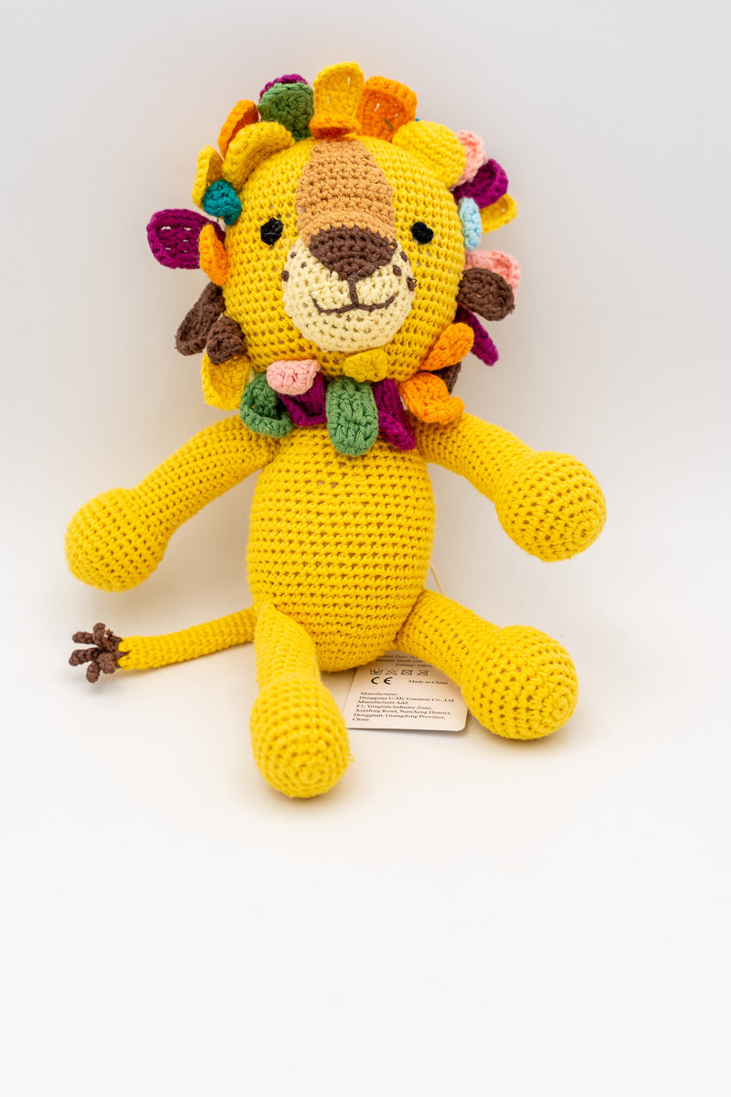 Peluche de león de crochet amarillo sentado con etiqueta de fabricante visible.