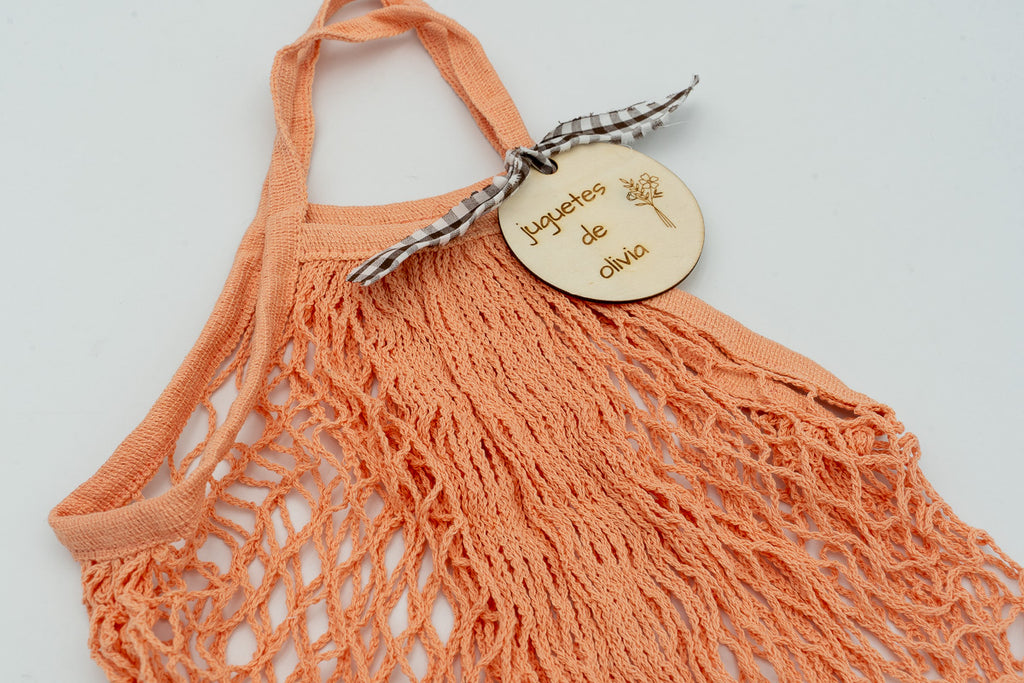 Detalle de bolsa naranja con placa de madera personalizada y lazo de cuadros marrones.