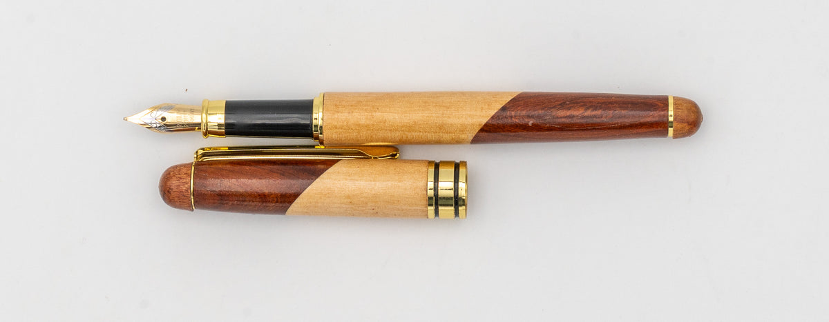 Detalle lateral de una pluma estilográfica de madera bicolor con plumín y tapa con clip dorado.
