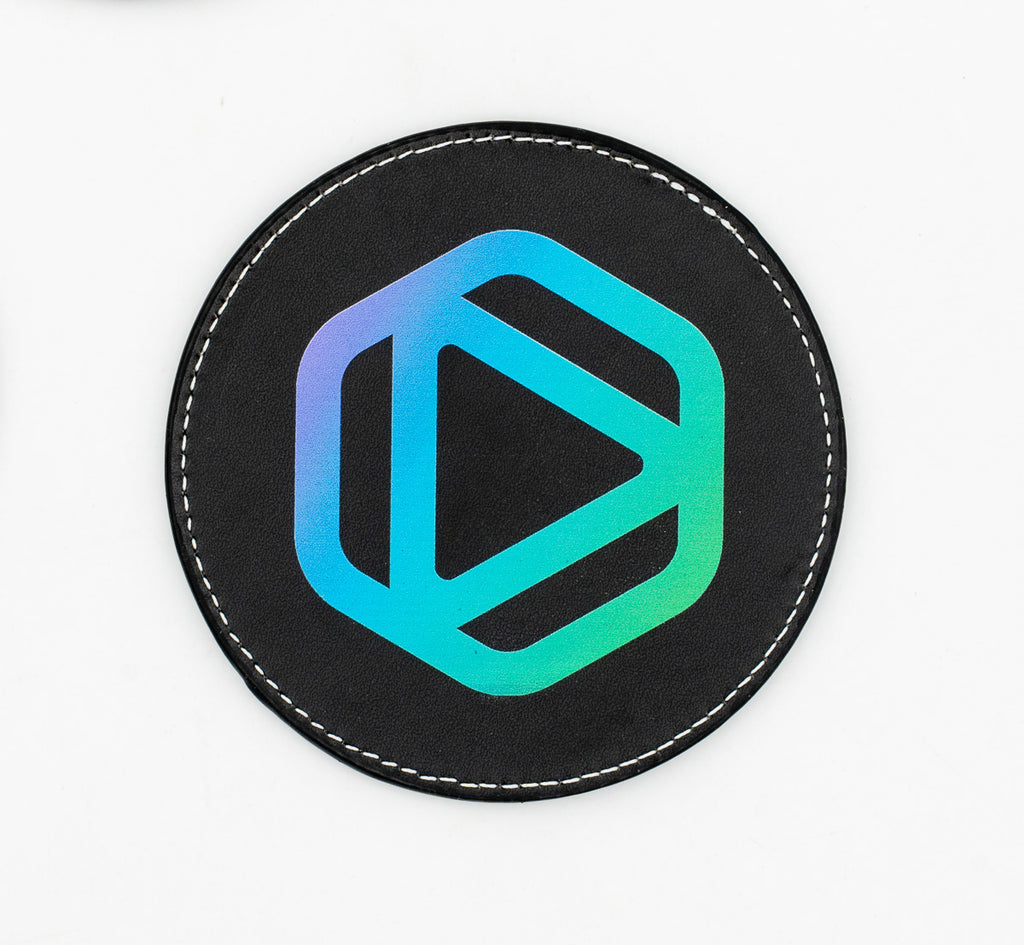 Posavasos redondo negro con emblema geométrico azul y verde.
