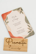 Invitación de boda de madera con hojas en tonos terracota y verde salvia