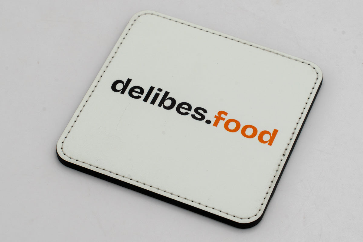 Posavasos cuadrado blanco con logotipo delibes.Food negro y naranja.