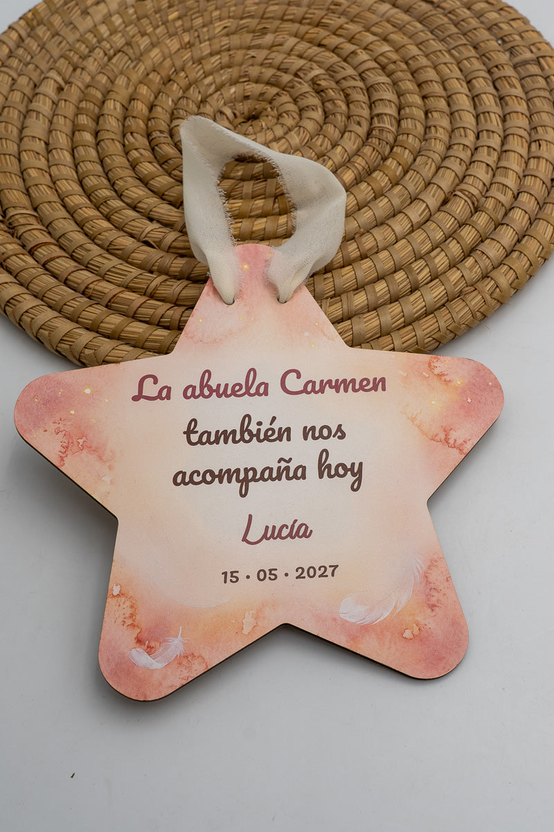 Estrella de comunión con fondo de acuarela rosa y plumas blancas, la frase «La abuela Carmen también nos acompaña hoy», el nombre de ejemplo Lucía y la fecha, con cinta crema.