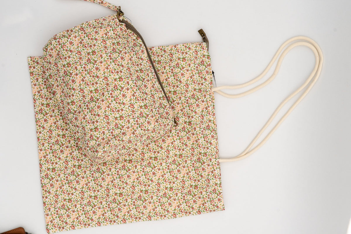 Neceser sobre unha bolsa de tea con estampado de flores cor pexego e follas verdes.