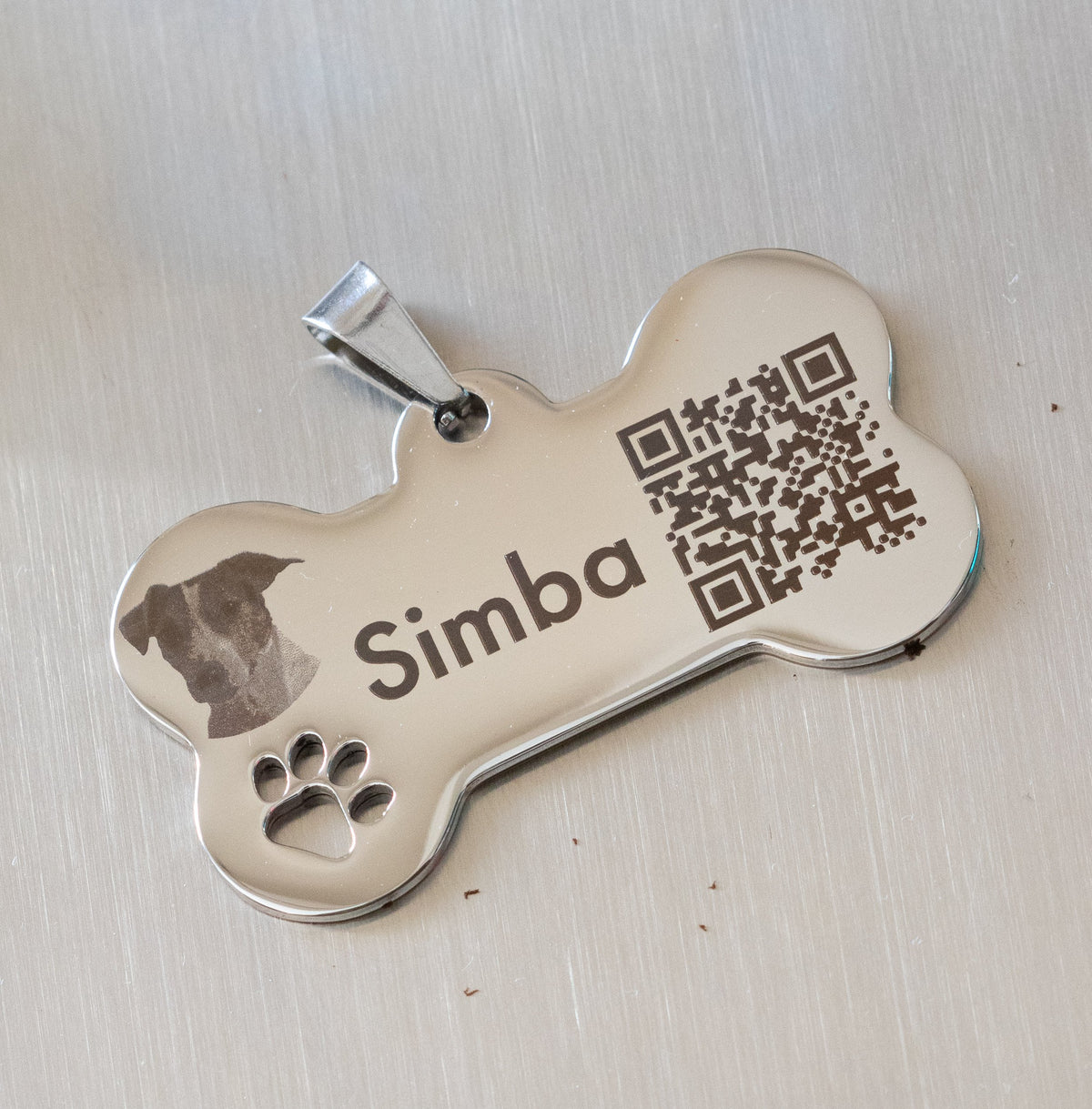 Chapa de acero inoxidable en forma de hueso con grabado de perro Simba y código QR funcional.