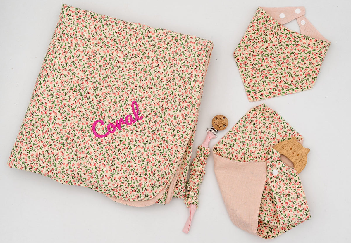 Conxunto rosa con manta de flores e o nome Coral bordado, babeiro bandana, muselina rosa con mordedor de madeira e suxeitachupetas.