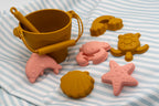 Varietat de motlles marins de silicona de colors mostassa i rosa sobre un fons de ratlles.