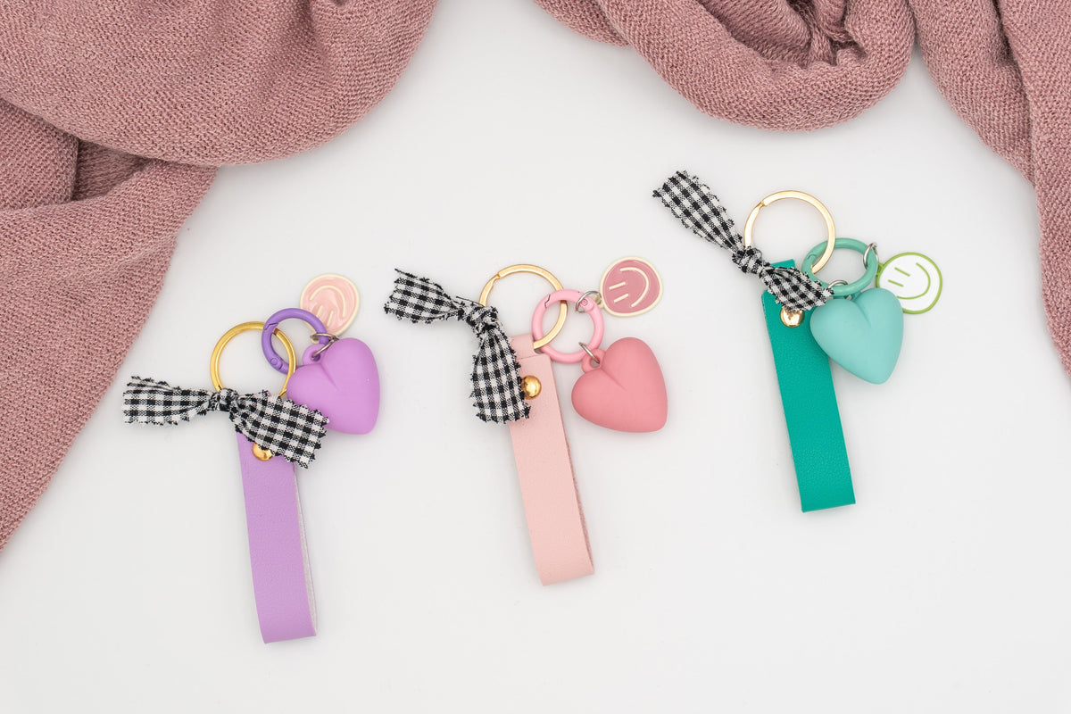 Tres llaveros personalizados en colores púrpura, rosa y aguamarina con charms y anillas doradas.