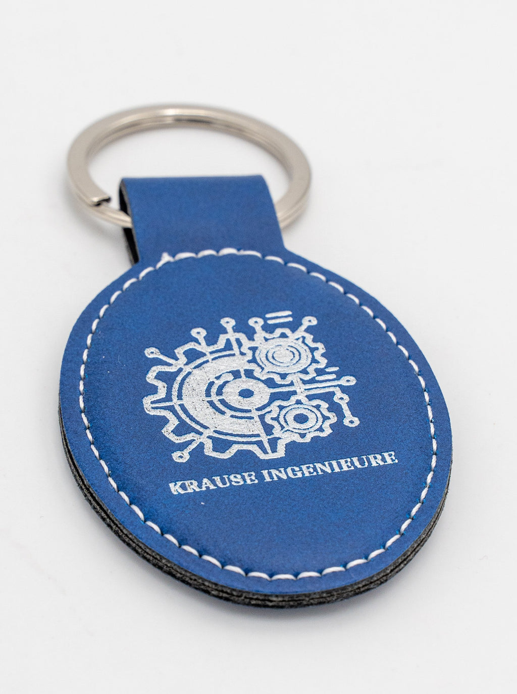 Clauer ovalat blau amb logotip clar i costura blanca.