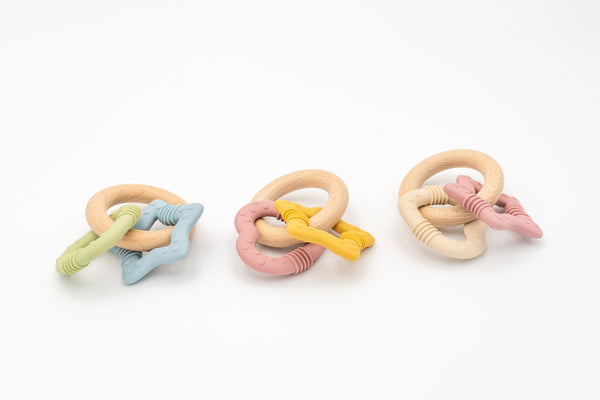 Tres juegos de mordedores para bebé compuestos por aros de madera de haya y piezas de silicona texturizadas en colores pastel.