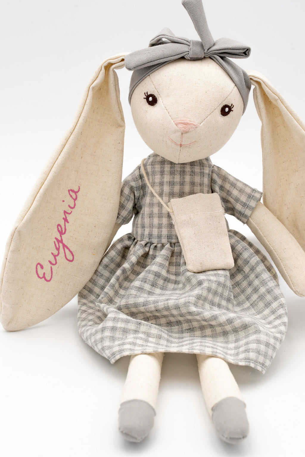 Vista frontal de la conejita gris personalizada con Eugenia, lazo gris y largas orejas de algodón.