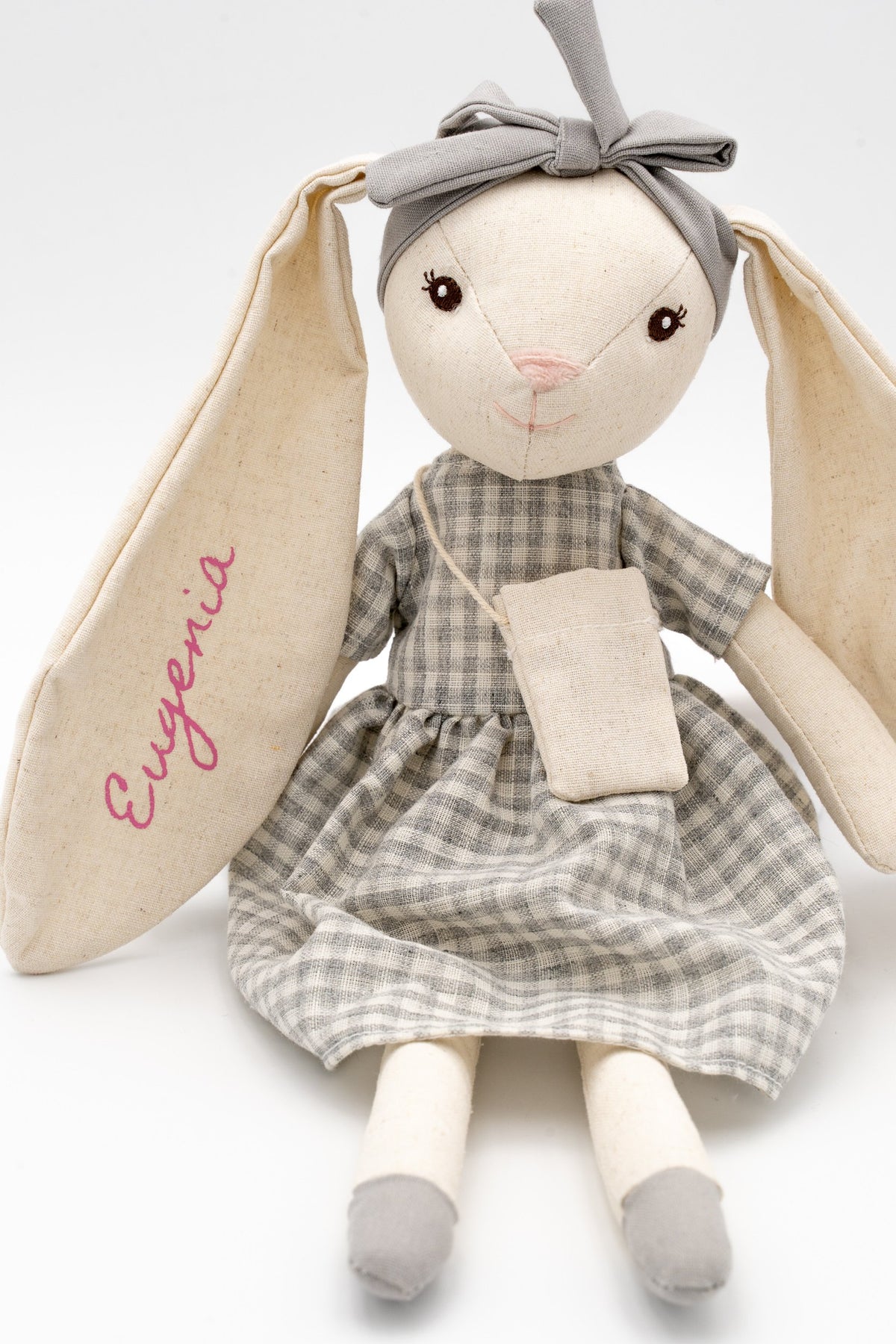 Vista frontal de la conejita gris personalizada con Eugenia, lazo gris y largas orejas de algodón.