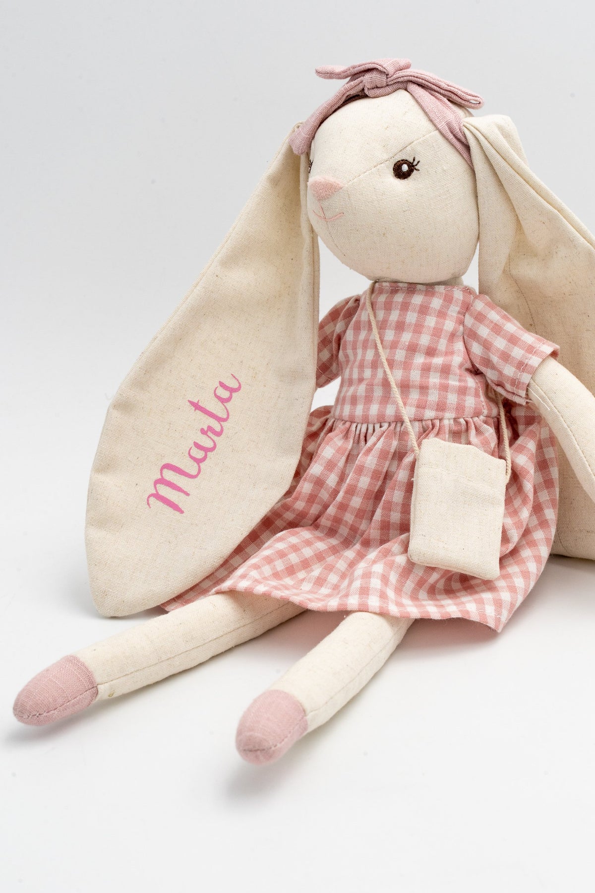 Coelliña de trapo rosa sentada, co nome Marta nunha orella, vestido vichy e bolso de tea.