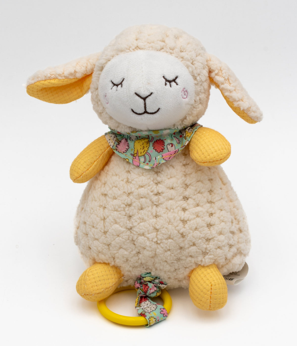 Peluche musical con forma de ovejita cruda y amarilla, pañuelo estampado y anilla inferior.