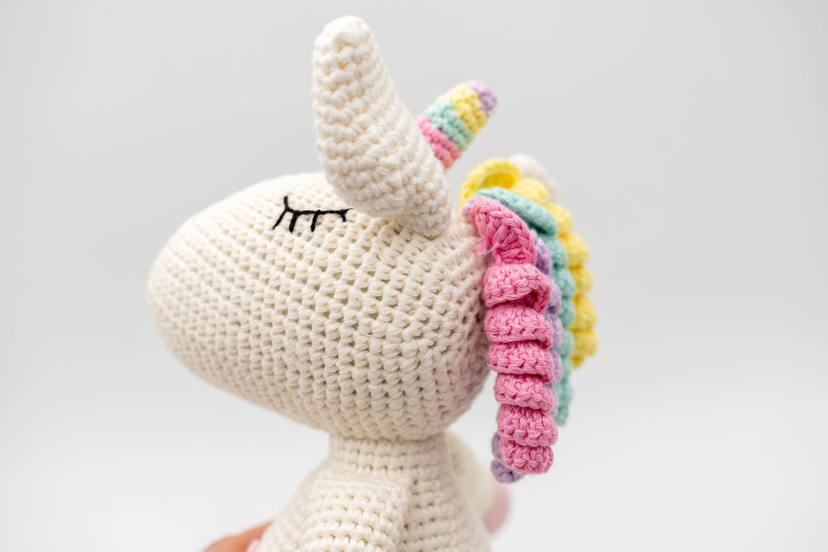 Perfil da cabeza dun unicornio branco de croché que mostra o corno e a melena en espiral.