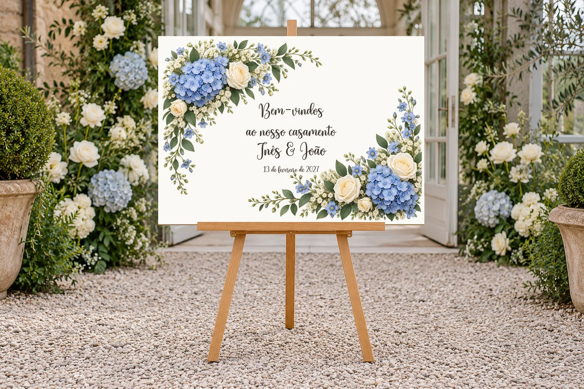 Cartel de bienvenida de boda A3 a color con hortensias azules y rosas blancas, texto en portugués y caballete en una entrada ajardinada.