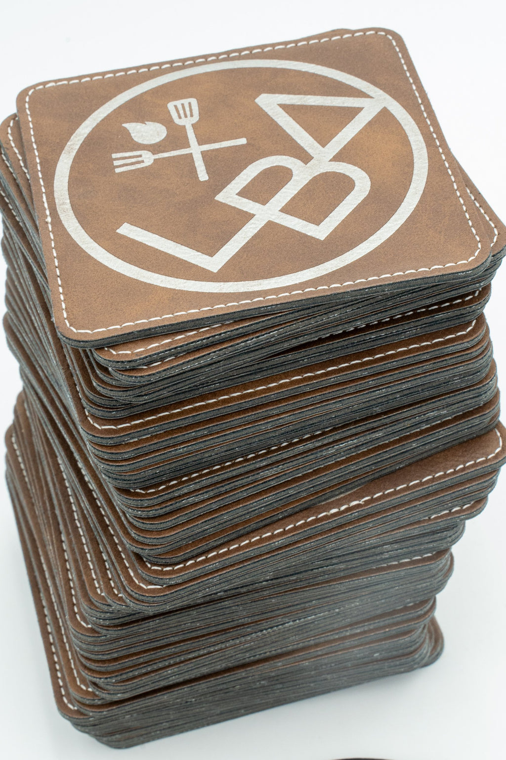 Pila de posavasos cadrados marróns con logotipo branco e costura no contorno.