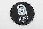 Posavasos redondo negro con logotipo conmemorativo de cen anos en branco.