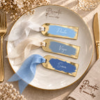 Tres marcasitios de metacrilato espejo dorado en azul cielo, azul grisáceo y azul tinta, con cintas chiffon coordinadas, sobre plato Picasita.