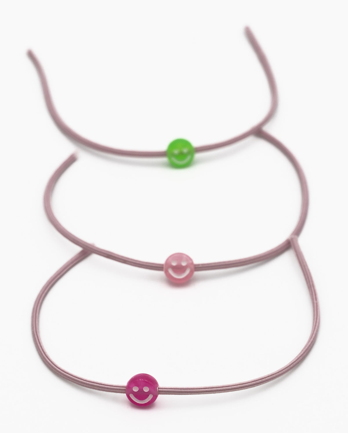 Tres pulseiras elásticas malva con contas de silicona en forma de sorriso verde e rosa.