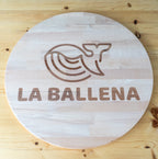 Tablero redondo de madera con una ballena y el nombre La Ballena grabados.