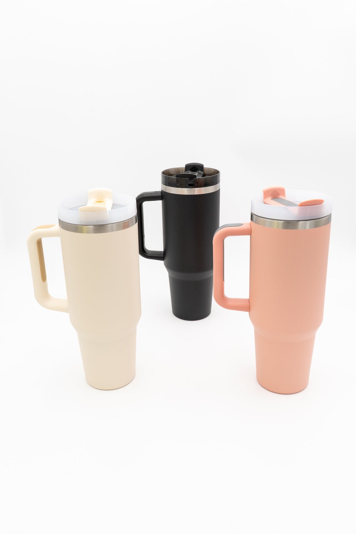 Tres vasos térmicos con asa nas cores crema, negra e salmón sobre fondo branco.