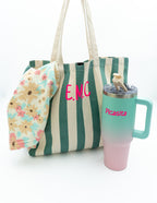 Bolso de praia verde xunto a unha botella térmica e unha toalla con estampado floral.