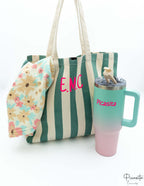 Bolso de playa verde junto a una botella térmica y una toalla con estampado floral.