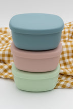 Tuppers de silicona apilados en azul gris, rosa y verde claro