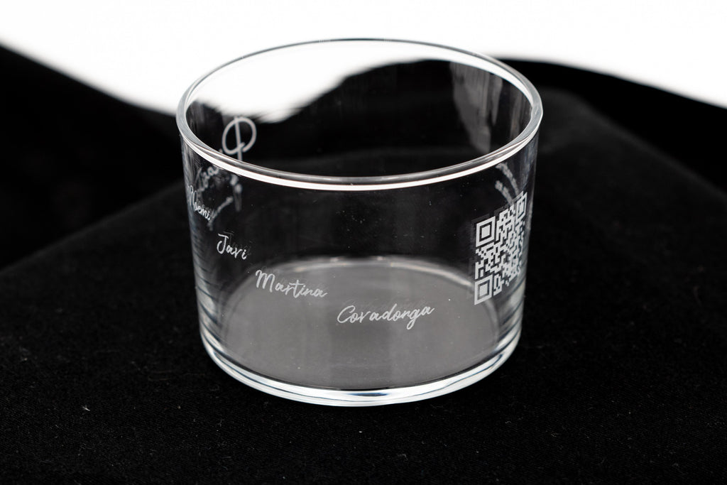 Vaso de cristal transparente con nombres grabados en cursiva sobre una superficie oscura elegante.